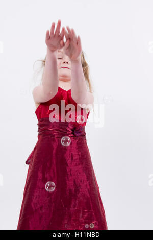 Junge Mädchen tragen glänzende rote Abendkleid spielen fangen und popping bubbles, Studioportrait isoliert auf weiss Stockfoto