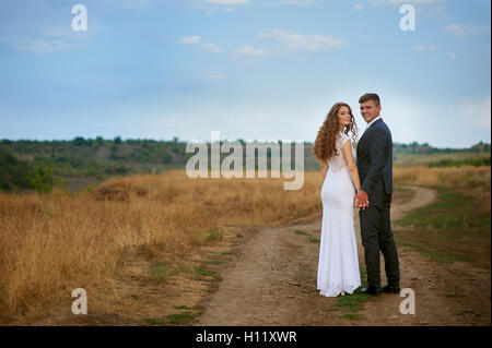 Braut und Bräutigam zu Fuß auf der Straße in einem Feld Stockfoto