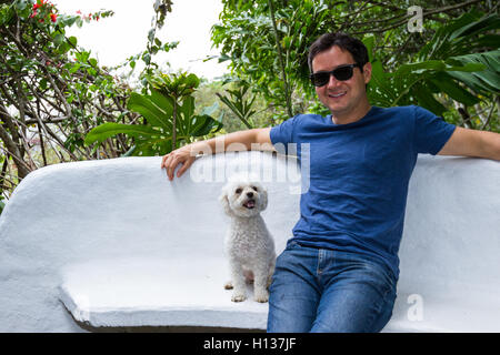 Porträt eines Mannes sitzen auf einer Bank mit seinem besten Freund, einen weißen Mini Toypudel Stockfoto