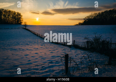 Winter-Sonnenuntergang über einen Zaun und Schnee überdachten Hof-Feld im ländlichen Carroll County, Maryland. Stockfoto