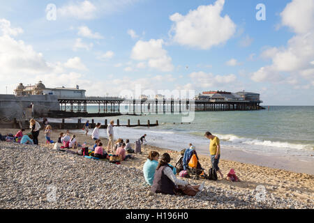 Englischer Sommer; Leute sitzen am Cromer Strand, mit Cromer Pier, Cromer, Nord Norfolk Küste, Norfolk UK Stockfoto