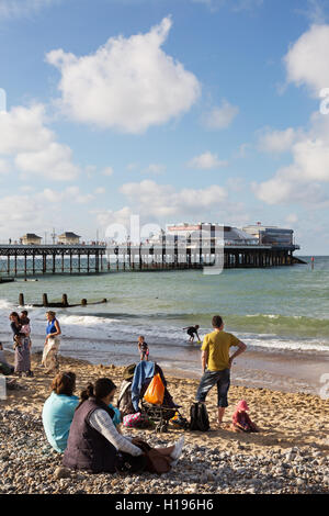 Leute sitzen am Strand von Cromer, mit Norfolk Küste Cromer Pier, Cromer, North Norfolk UK Stockfoto