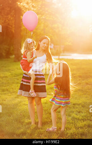 Mutter und zwei Töchter für einen Spaziergang im Park. Mutter hält Tochter auf Händen. Zeit mit der Familie zusammen. Fröhliches Picknick. Stockfoto