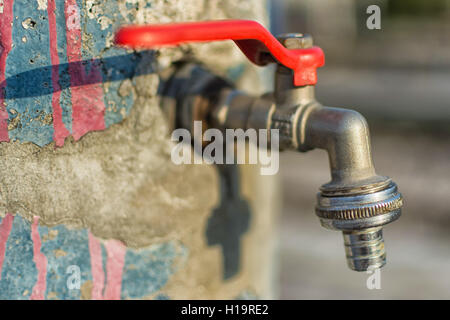 Wasserhahn auf alten geknackt blau gestrichenen Wand. Roter Griff Leitungswasser im freien Hintergrund. Sparen Sie Wasserkonzept. Stockfoto