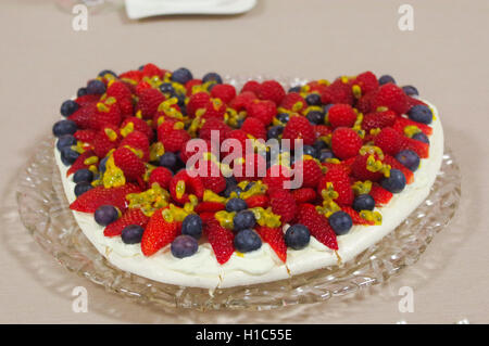 hausgemachte Kuchen mit Erdbeeren und Heidelbeeren für den Valentinstag in Herzform auf ein Glas Platte Tischdecke Stockfoto