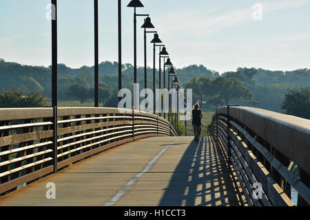 Ein Läufer überquert die Spottdrossel Punkt Fußgängerbrücke bei Sonnenaufgang am nördlichen Ende des White Rock Lake in Dallas. Stockfoto