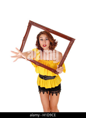 Eine böse Frau in eine gelbe Bluse und schwarzen Hosen dehnen ihre Hand Trog einen Bilderrahmen für weißen Hintergrund isoliert. Stockfoto