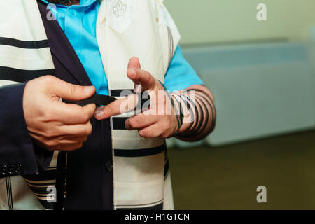 Jüdischer Mann eingewickelt in Tefillin beten. Ein religiöser orthodoxer Jude mit Arm-Tefillin auf seiner linken Hand betet Stockfoto