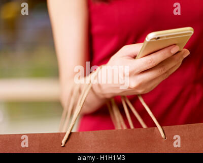 Hand einer jungen Frau, die Einkaufstaschen mit Handy Stockfoto