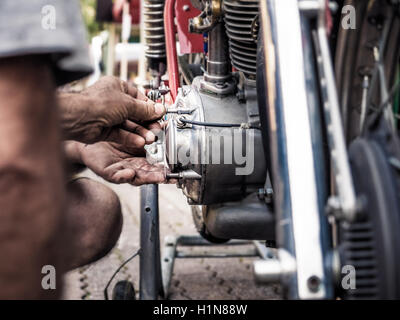 Mechaniker mit schmutzigen Händen Befestigungsschraube auf einem alten Fahrrad Motor, absichtlichen Unschärfe und lebendige Farben. Stockfoto