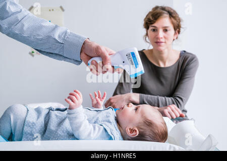 Überprüfen die Temperatur von einem 3 Monate alten Babymädchen mit Stirn-Thermometer. Stockfoto