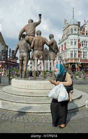 Muslimische Frau geht vorbei an den World Cup Skulptur auch genannt The Champions in der Nähe in der Nähe von West Ham United Football Club alte Upton Park Stadion, mit Bobby Moore, Geoff Hurst, Martin Peters und Ray Wilson, Helden des Jahres 1966 Englands Sieg im Wembley-Stadion. London.UK Stockfoto