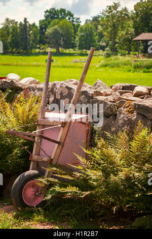 Bild von einer Schubkarre gegen ein Naturstein Wand in einer ländlichen Umgebung. Stockfoto