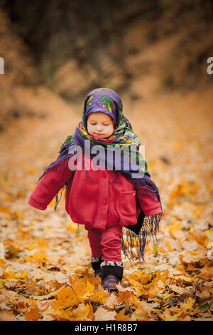 Kind Mädchen in ukrainischen Folklore Schal mit Blumendruck, auf Kopf zu Fuß auf Laub Stockfoto