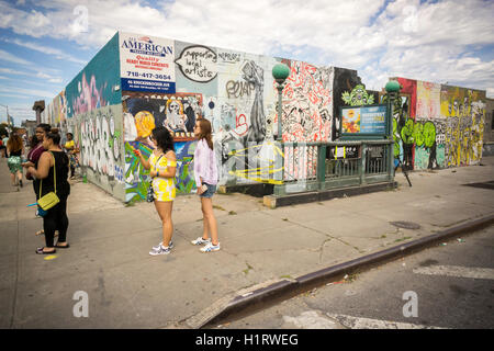 Besucher zu Fuß vorbei an Graffiti-Stil Wandmalereien im Stadtteil Bushwick, Brooklyn in New York auf Sonntag, 11. September 2016. Die Nachbarschaft hat Gentrifizierung der Wechsel von einer rauen und Wäschetrockner Mischung von Hispanic und von Industrie, eine Oase für Hipster, zwingt viele alteingesessene, wegen der steigenden mieten. (© Richard B. Levine) Stockfoto