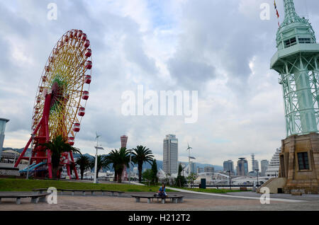 Thai Frau im Park zwischen Leuchtturm und Riesenräder mit klassischen Gebäude und Wahrzeichen Kobe Port Tower am Kob Stockfoto