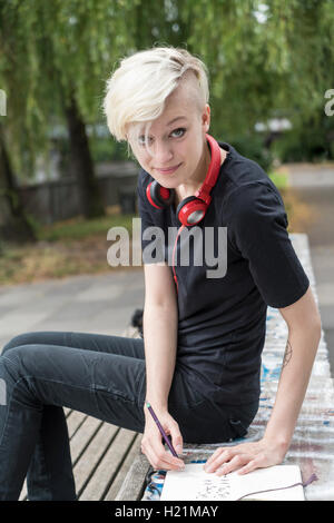 Porträt der lächelnde junge Frau mit Kopfhörern auf Parkbank Stockfoto