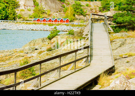 Holzsteg am felsigen Ufer an der schwedischen Westküste im Frühherbst. Roten Hausboote in der Ferne. Stockfoto