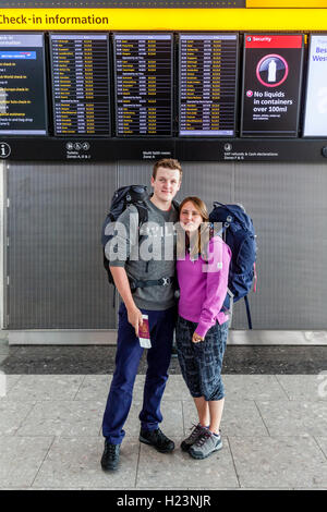 Ein Rucksack paar Pose vor die Abfahrtstafel am Flughafen Heathrow Terminal 5, London, UK Stockfoto