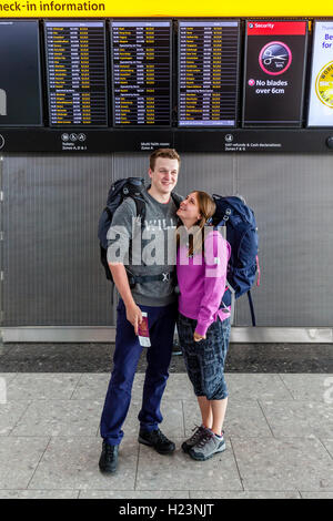 Ein Rucksack paar Pose vor die Abfahrtstafel am Flughafen Heathrow Terminal 5, London, UK Stockfoto