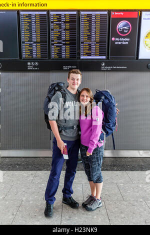 Ein Rucksack paar Pose vor die Abfahrtstafel am Flughafen Heathrow Terminal 5, London, UK Stockfoto