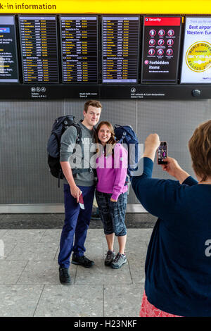 Ein Rucksack paar Pose vor die Abfahrtstafel am Flughafen Heathrow Terminal 5, London, UK Stockfoto