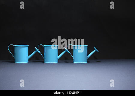 Drei blaue Gießkannen in Folge auf dunklem Hintergrund Stockfoto