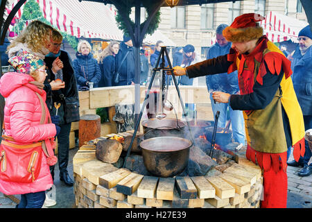 Riga, Lettland - 26. Dezember 2015: Zufällige Personen genießen Sie eine traditionelle Mahlzeit in der Nähe der riesigen Topf auf dem Weihnachtsmarkt in Riga. Es ist der älteste Weihnachtsmarkt in Lettland und dort jedes Jahr stattfindet. Stockfoto