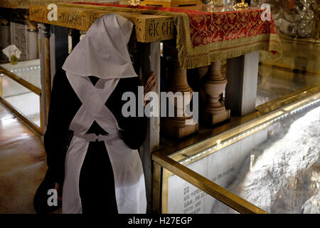Eine orthodoxe Nonne kniet vor dem Altar der Kreuzigung auf der linken Seite des Kalvariums oder Golgatha, der traditionell als Ort der Kreuzigung Jesu gilt. Der Hauptaltar gehört zum griechisch-orthodoxen Altar, der den Felsen des Kalvarienfeldes in der 12. Station des Kreuzes in der Grabeskirche in der Altstadt von Jerusalem Israel enthält Stockfoto