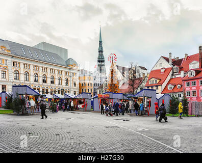 Riga, Lettland - 26. Dezember 2015: Menschen auf dem Weihnachtsmarkt mit St. Peter Church Turm befindet sich auf dem Livu-Platz im Zentrum der Altstadt von Riga, Lettland. Stockfoto