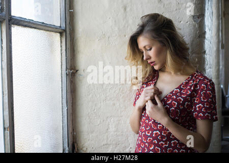 Schöne junge Frau im roten Kleid am Fenster übergibt Herz Stockfoto