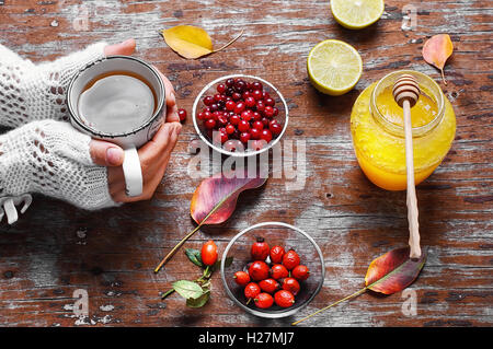 Tasse in der Hand mit herbstlichen Beeren Tee und Glas Honig Stockfoto