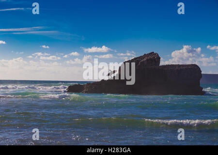 Unbekannter Mann mit Surfbrett auf großen Berg Felsen am Tonel Strand, Sagres, Portugal Stockfoto