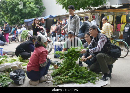 Ha Noi, Vietnam - 3. Dezember 2015: Reisende fordern für den Kauf von grünem Gemüse auf einem Straßenmarkt in Vietnam Stockfoto