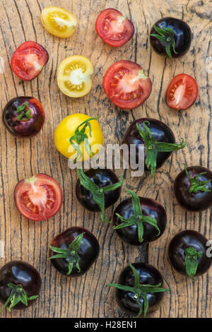 Gelbe Tomaten und schwarze Tomaten Indigo Rose ganze und halbierte auf Holz Stockfoto