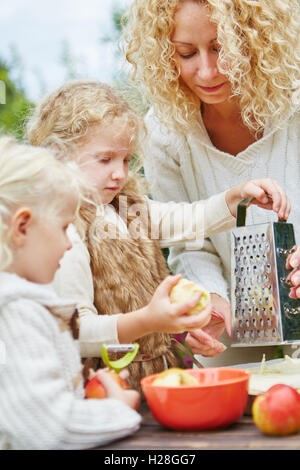 Mutter und zwei Mädchen reiben Äpfel zusammen für einen Kuchen Stockfoto