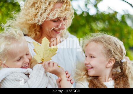 Schwestern und Mutter mit Herbstlaub in der Natur spielen Stockfoto