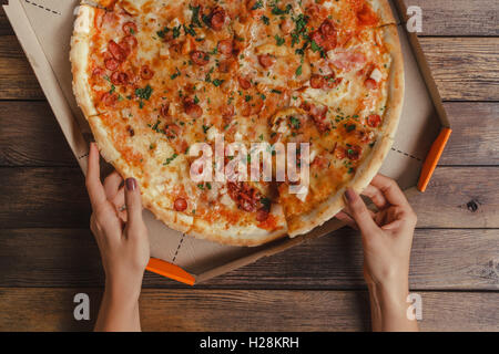 Weibliche Hände unter Stück Pizza Stockfoto