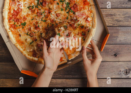 Weibliche Hände unter Stück Pizza Stockfoto