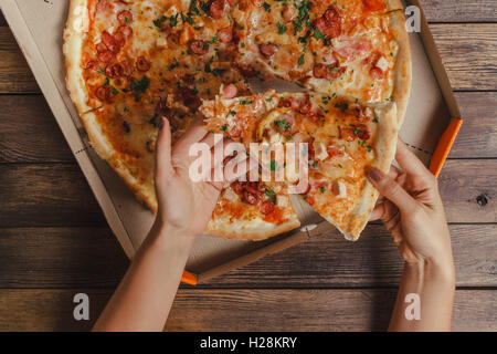 Weibliche Hände unter Stück Pizza Stockfoto