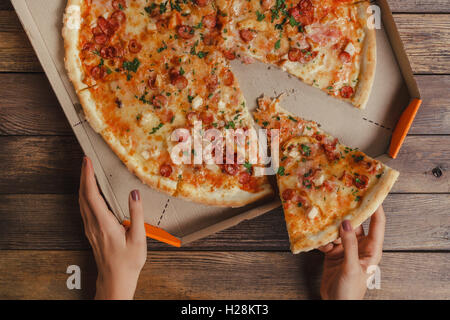 Weibliche Hände unter Stück Pizza Stockfoto