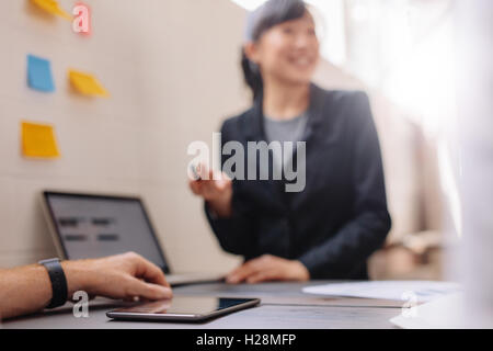 Schuss des jungen Mannes Hand mit digital-Tablette auf Tisch mit Kollegin geben Präsentation auf Laptop hautnah. Stockfoto