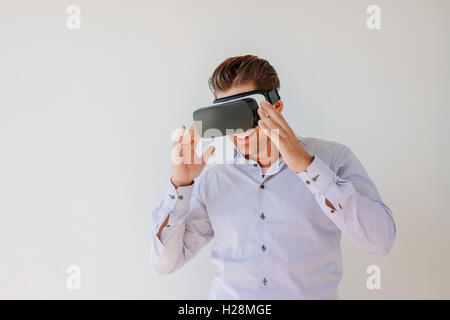 Schuss von glücklich Geschäftsmann Uhren Inhalte auf einem virtual-Reality-Display. Geschäftsmann mit virtual Reality Brille gegen grauen ba Stockfoto