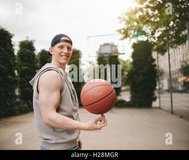 Porträt von teenage Streetball Spieler den Ball dreht und lächelt in die Kamera. Glücklich Jüngling Ausgleich Basketball auf seine Fi Stockfoto