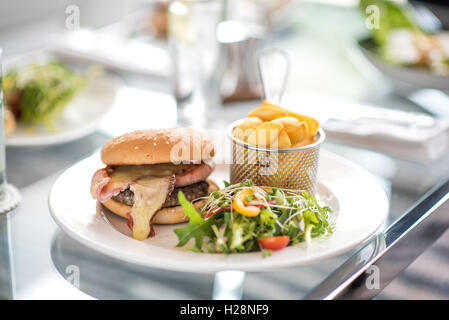 Ein Hamburger mit Käse und Schinken auf einem Teller mit Pommes Frites und Salat Stockfoto