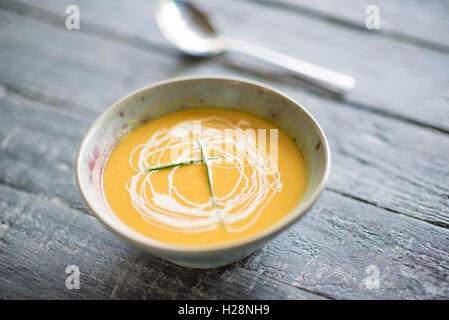 Karotten und Koriander-Suppe in einer handgefertigten Schüssel mit rustikaler Hintergrund Stockfoto