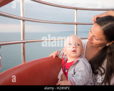 Junge Mutter mit ihrem kleinen Sohn spielen im Freien auf Riesenrad Stockfoto