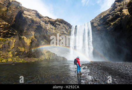 Wanderer vor der Skógafoss Wasserfalls, Regenbogen, Skogar, Region Süd, Island Stockfoto