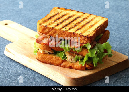 Club Sandwich mit Türkei, Speck, Schinken, Tomaten, Käse, Salat, und auf einem Holzbrett garniert Stockfoto