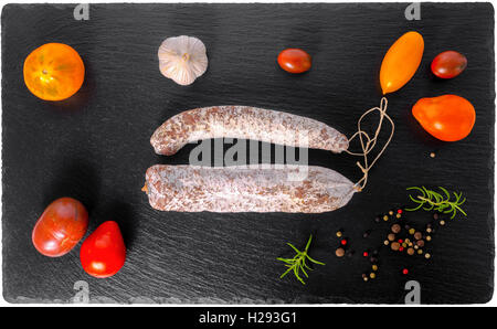 lecker lecker geräucherten Dauerwürste, dünne Salami und rot, gelb, Tomaten, Knoblauch, Paprika, Rosmarin auf Schiefer Hintergrund, clos Stockfoto